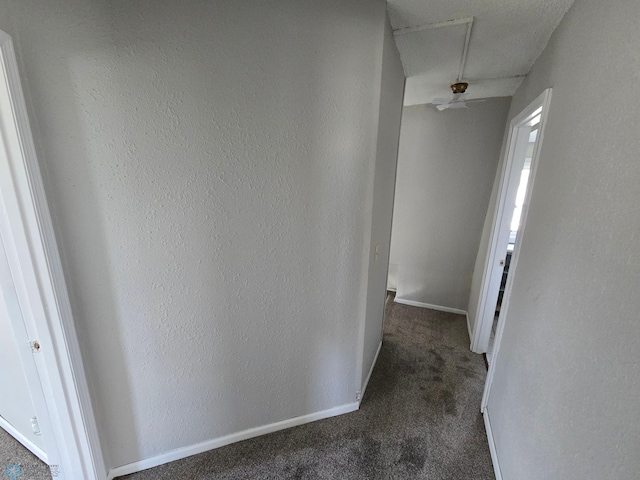 hallway with dark carpet and baseboards