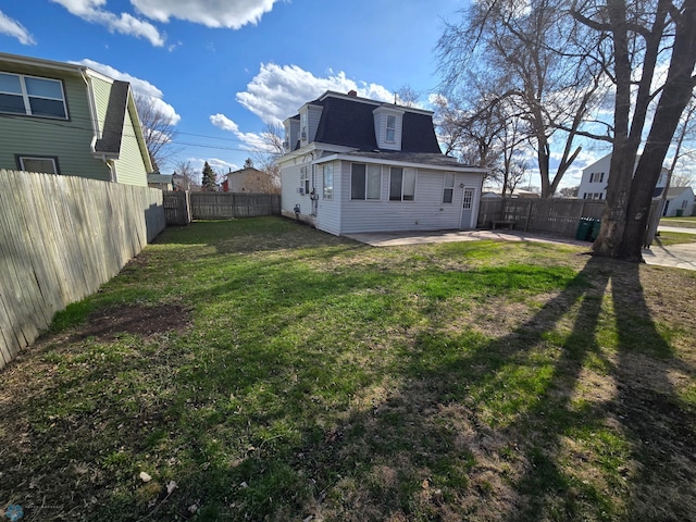 back of house featuring a shingled roof, a patio area, a fenced backyard, a lawn, and mansard roof