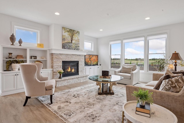 living room with a stone fireplace, recessed lighting, and light wood-style flooring