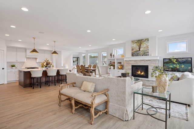 living area with recessed lighting, light wood-style flooring, and a stone fireplace