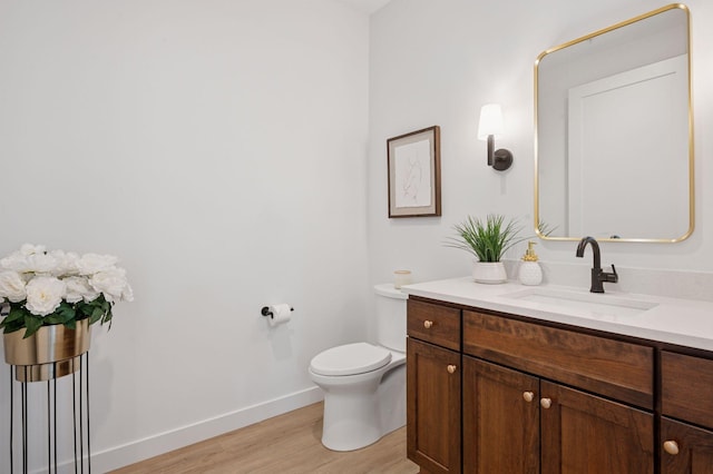 half bath with baseboards, vanity, toilet, and wood finished floors