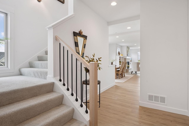 stairway with a healthy amount of sunlight, visible vents, wood finished floors, baseboards, and recessed lighting