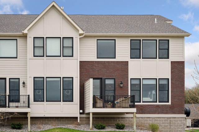 rear view of property with a shingled roof and brick siding