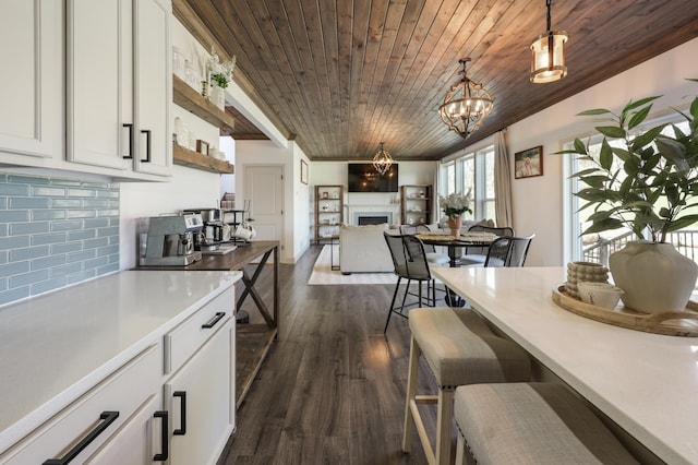 kitchen featuring pendant lighting, a fireplace, dark wood finished floors, wooden ceiling, and white cabinetry