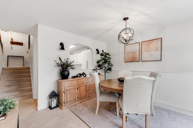 dining room with arched walkways, an inviting chandelier, stairs, light colored carpet, and baseboards