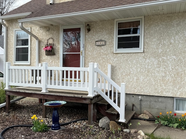entrance to property featuring a shingled roof and stucco siding