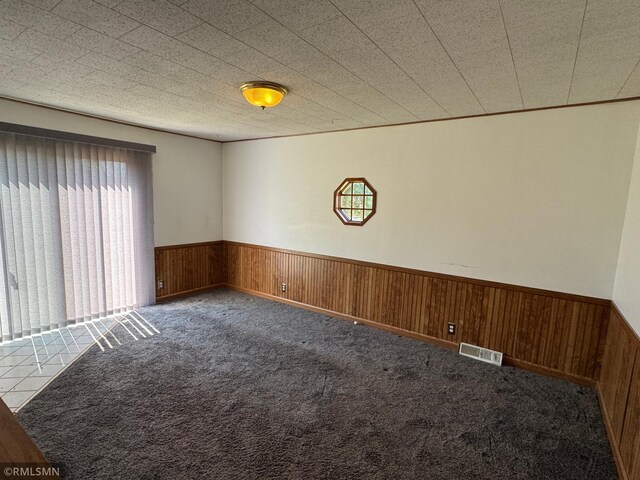 carpeted spare room featuring wooden walls, visible vents, and wainscoting