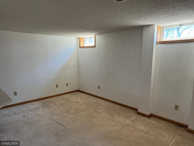 below grade area featuring a textured ceiling, carpet flooring, baseboards, and a healthy amount of sunlight