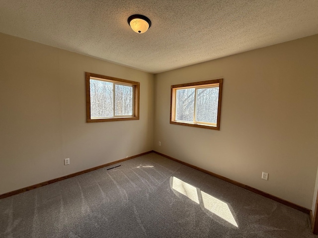 unfurnished room with a textured ceiling, visible vents, carpet flooring, and baseboards