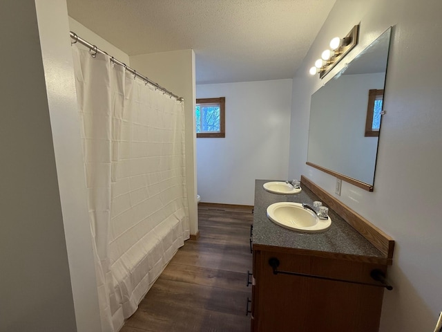 bathroom with wood finished floors, a textured ceiling, double vanity, and a sink