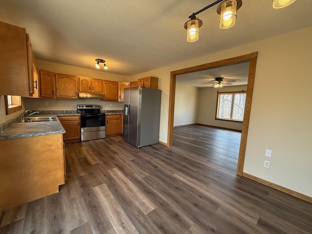 kitchen with a sink, under cabinet range hood, dark wood-type flooring, a textured ceiling, and appliances with stainless steel finishes