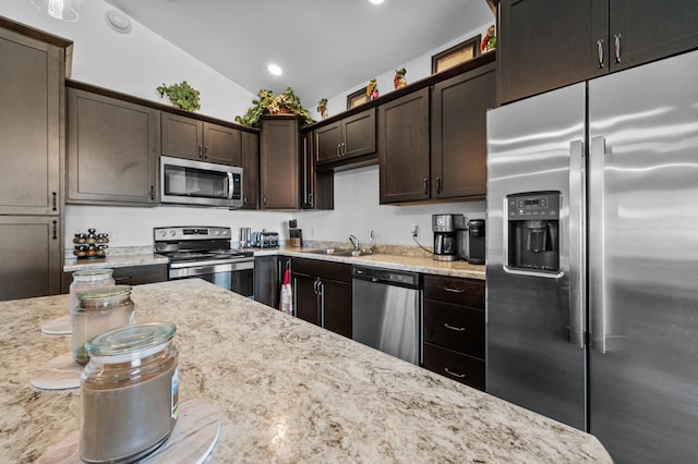 kitchen featuring dark brown cabinets, light stone countertops, a sink, stainless steel appliances, and vaulted ceiling
