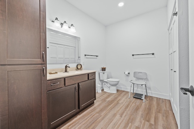 bathroom featuring vanity, wood finished floors, toilet, baseboards, and recessed lighting