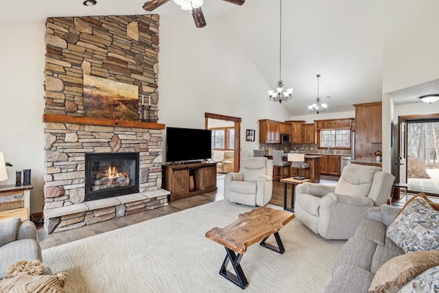 living area with light wood-style floors, high vaulted ceiling, a stone fireplace, and ceiling fan with notable chandelier