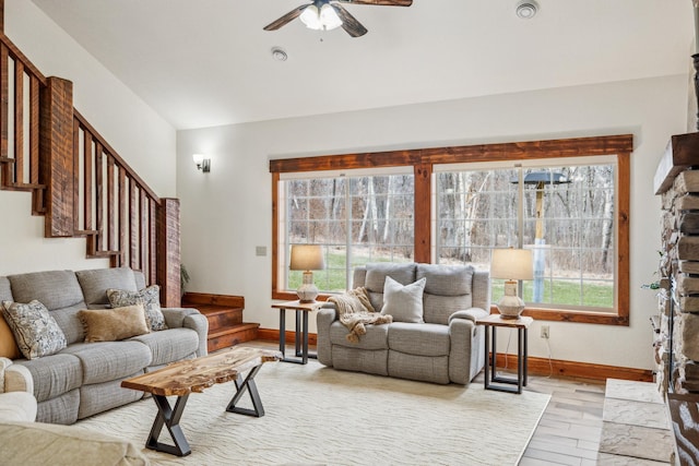 living area with stairway, light wood-style floors, ceiling fan, vaulted ceiling, and baseboards