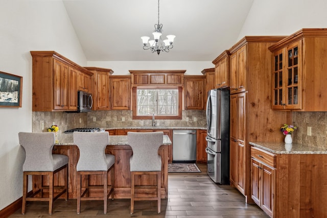 kitchen with brown cabinets, a chandelier, stainless steel appliances, a peninsula, and lofted ceiling