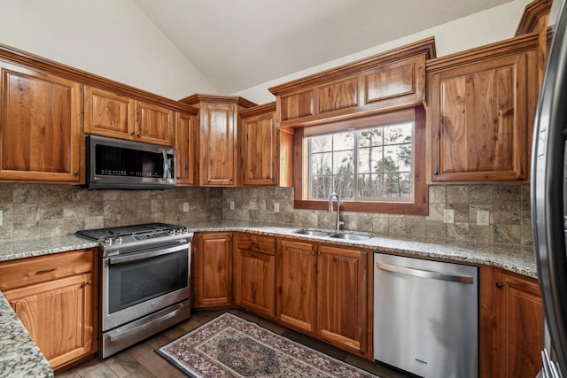 kitchen featuring tasteful backsplash, light stone countertops, stainless steel appliances, a sink, and lofted ceiling