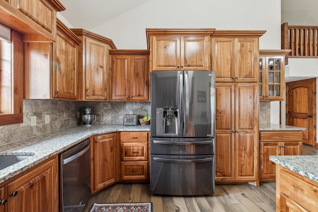 kitchen featuring light wood-type flooring, appliances with stainless steel finishes, brown cabinetry, and tasteful backsplash