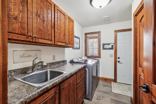 clothes washing area featuring a sink, cabinet space, washing machine and dryer, light wood-type flooring, and baseboards