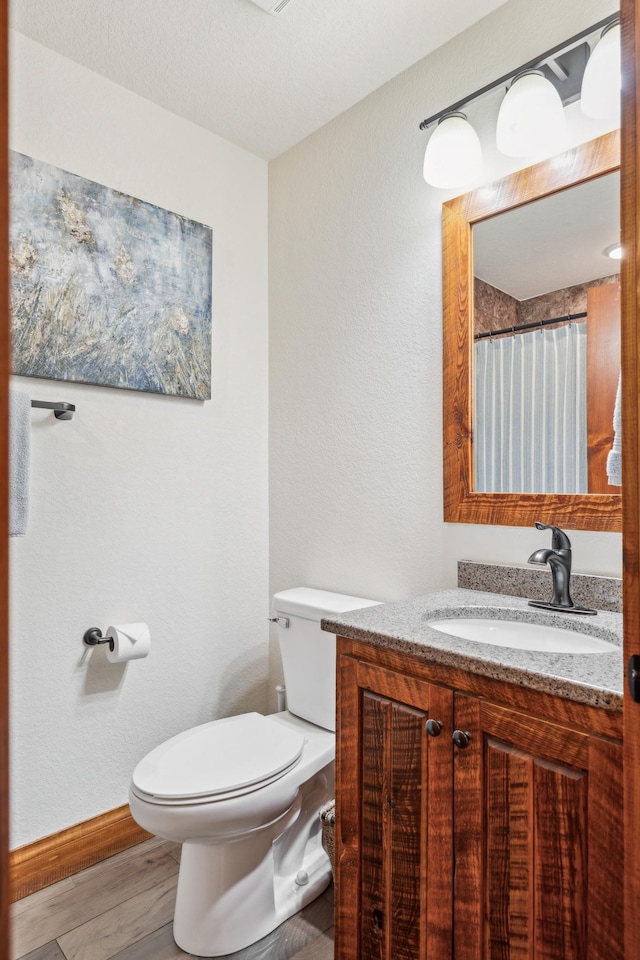 bathroom with wood finished floors, toilet, a textured wall, vanity, and baseboards