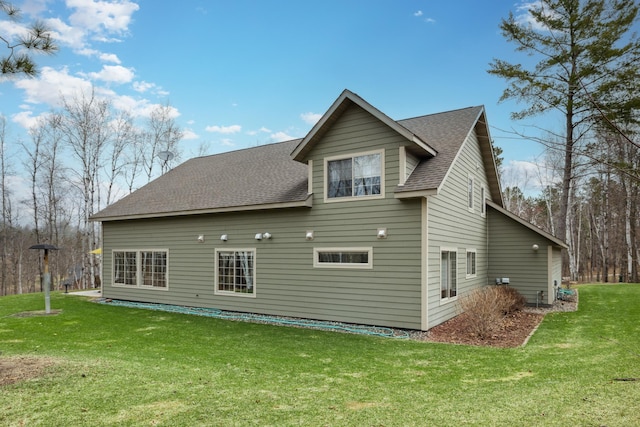 rear view of house with a lawn and roof with shingles