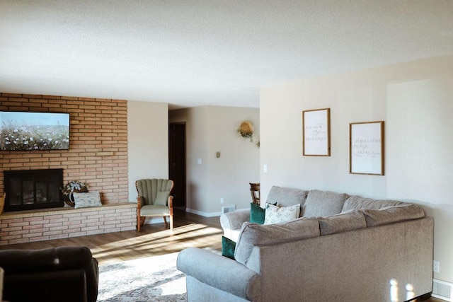 living room featuring a textured ceiling, a fireplace, wood finished floors, and visible vents