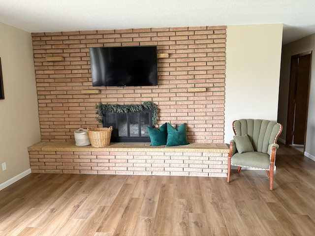 living room featuring baseboards, a brick fireplace, and wood finished floors