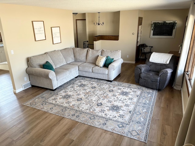 living room with visible vents, baseboards, wood finished floors, and a notable chandelier
