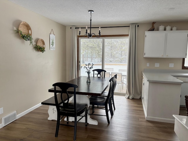 dining space with a textured ceiling, a chandelier, dark wood finished floors, baseboards, and visible vents