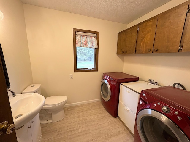 laundry area featuring laundry area, baseboards, washer and clothes dryer, a textured ceiling, and a sink