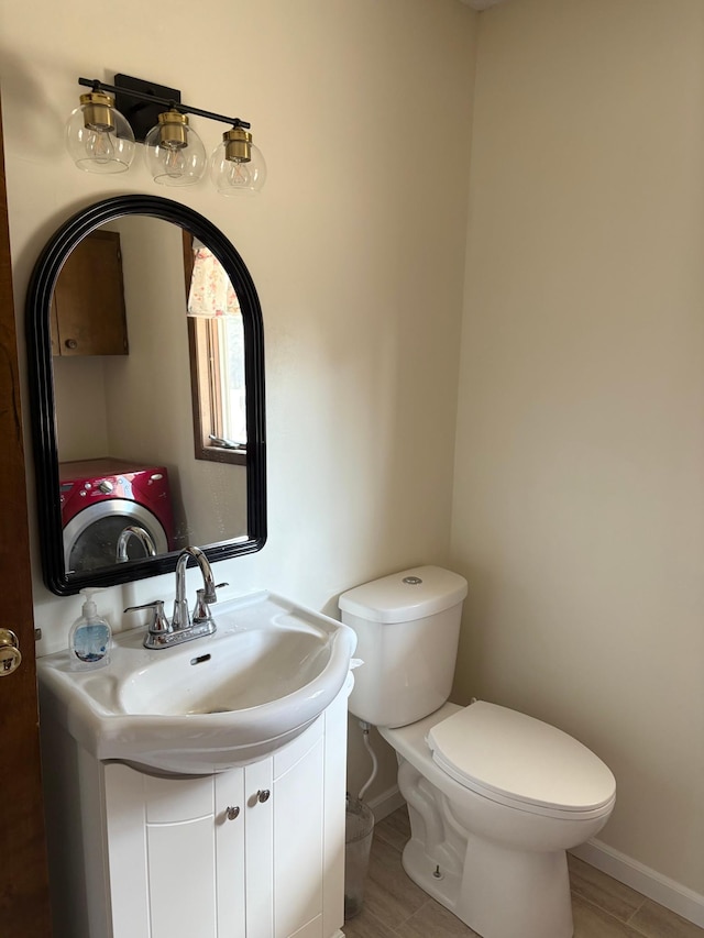 half bathroom with toilet, baseboards, washer / dryer, and vanity