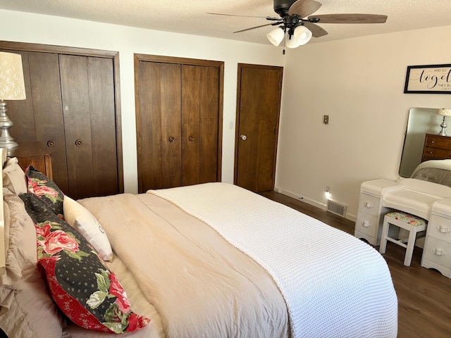 bedroom featuring ceiling fan, two closets, baseboards, visible vents, and dark wood-style floors