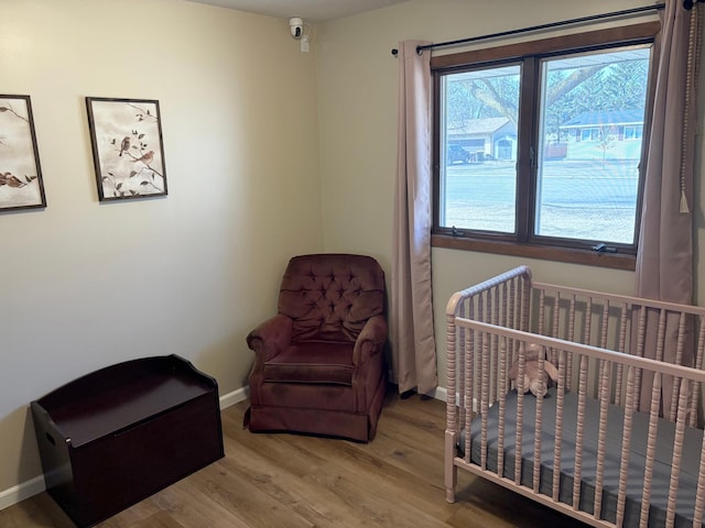 bedroom with baseboards, light wood-style flooring, and a crib