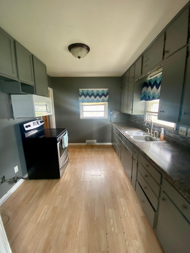 kitchen with stainless steel range with electric stovetop, a sink, light wood-style floors, green cabinets, and white microwave