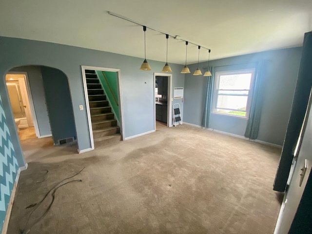 unfurnished living room featuring track lighting, stairway, baseboards, and arched walkways