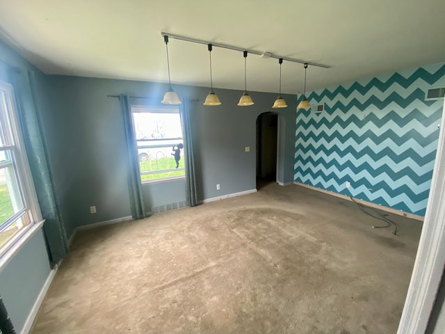 empty room featuring track lighting, baseboards, light carpet, and arched walkways