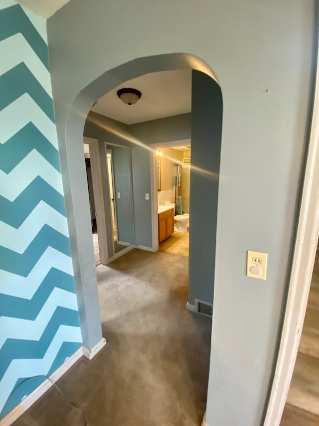 hallway with baseboards, arched walkways, and light colored carpet