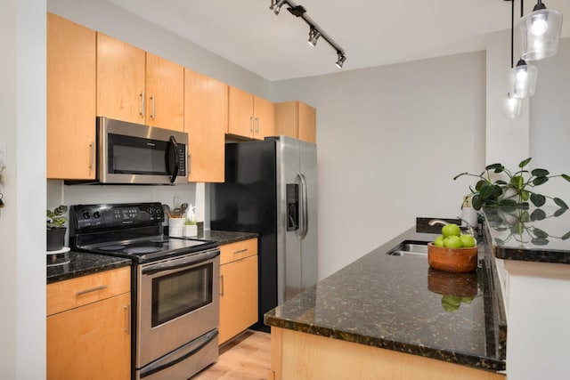 kitchen with stainless steel appliances, a sink, dark stone counters, and light wood finished floors