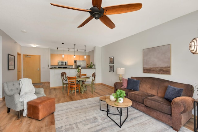 living room featuring light wood-style flooring, ceiling fan, baseboards, and track lighting