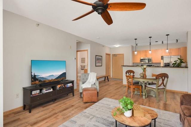living room with light wood-style flooring, ceiling fan, and baseboards