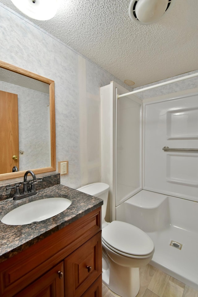 full bath featuring toilet, vanity, a textured ceiling, and a shower stall