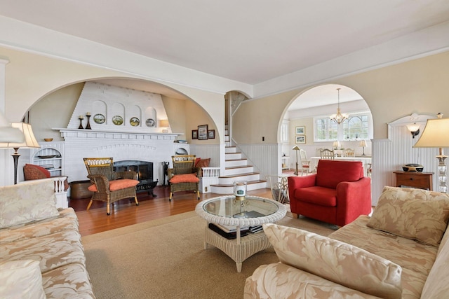 living room featuring a brick fireplace, wood finished floors, a chandelier, and stairway