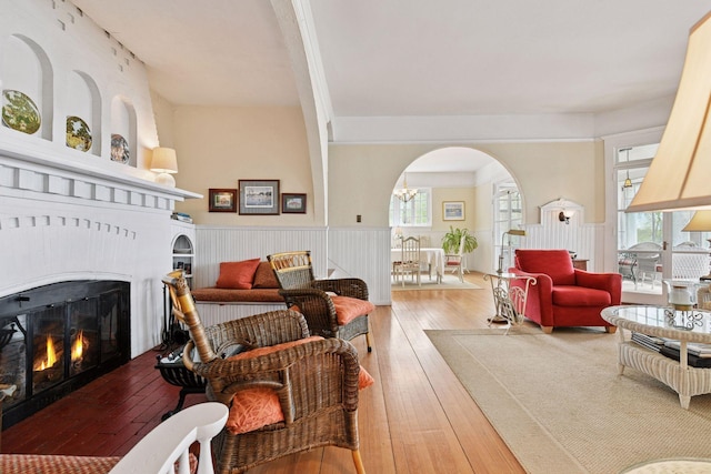 living area with a notable chandelier, wainscoting, arched walkways, hardwood / wood-style floors, and a lit fireplace