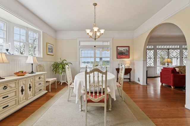 dining area featuring arched walkways, a notable chandelier, a healthy amount of sunlight, and a wainscoted wall