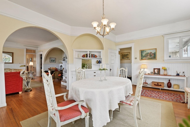 dining space featuring arched walkways, a wainscoted wall, wood finished floors, and a notable chandelier