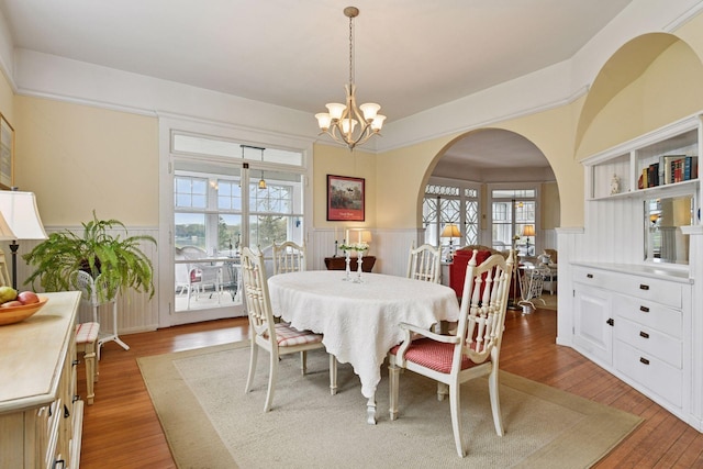 dining area featuring arched walkways, wainscoting, light wood-style flooring, and a notable chandelier