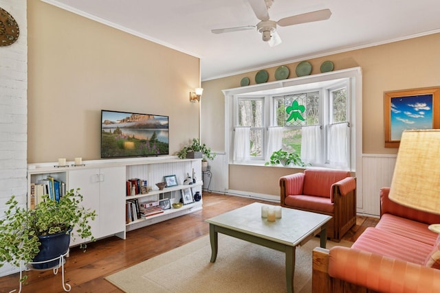 living area featuring crown molding, a ceiling fan, wainscoting, and wood finished floors