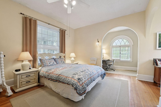bedroom featuring baseboards, arched walkways, a ceiling fan, and wood finished floors
