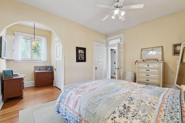 bedroom with arched walkways, baseboards, a ceiling fan, and light wood-style floors