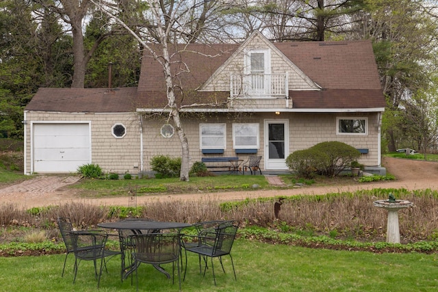 view of front of house with a shingled roof, a balcony, a front yard, and a garage